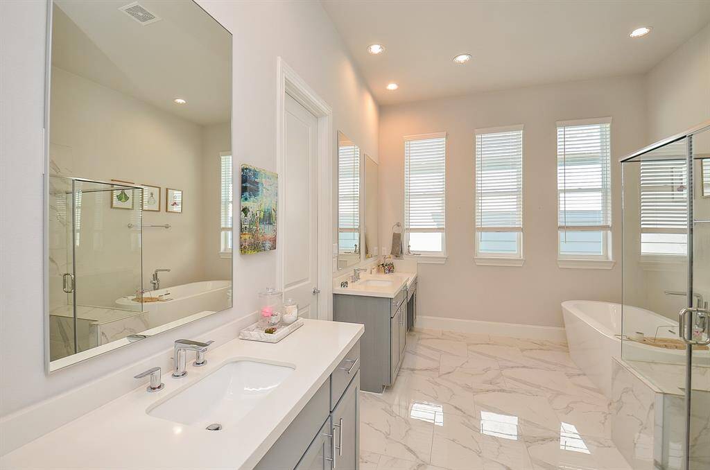 The primary bathroom has beautiful tile flooring, wall of windows and gray cabinets with Quartz counter tops.