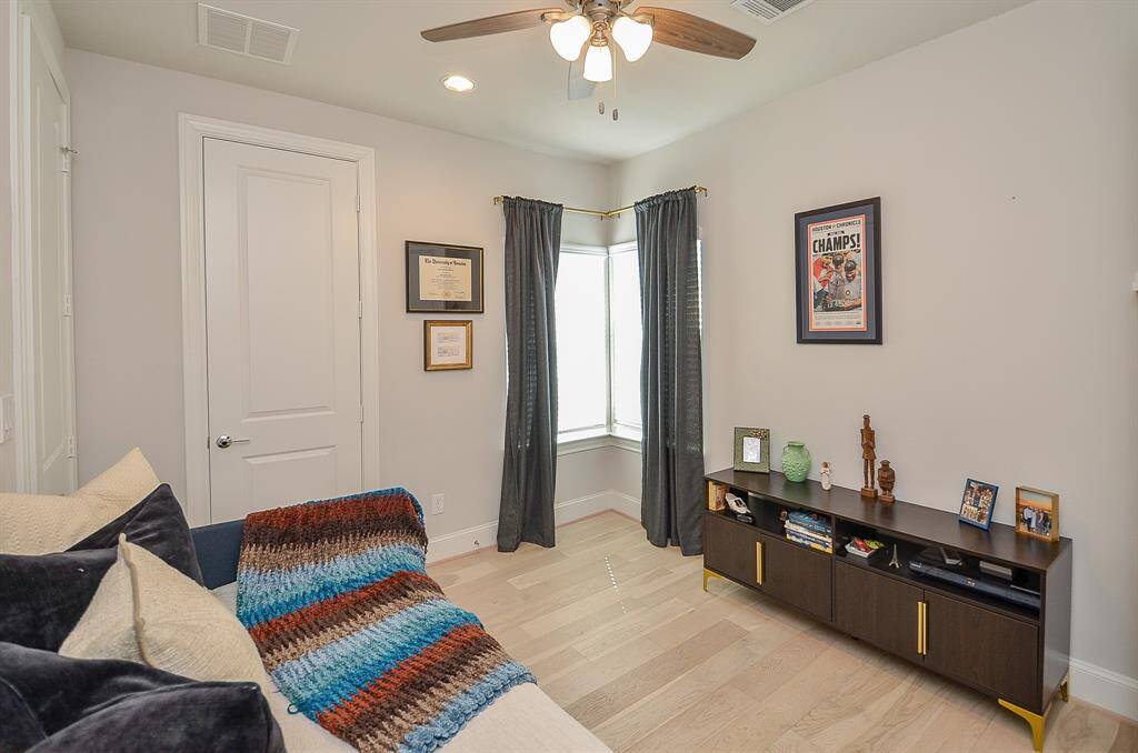 Secondary bedroom boasts walk in closet, wood flooring, brushed gold drape rods, accent panels and ceiling fan.