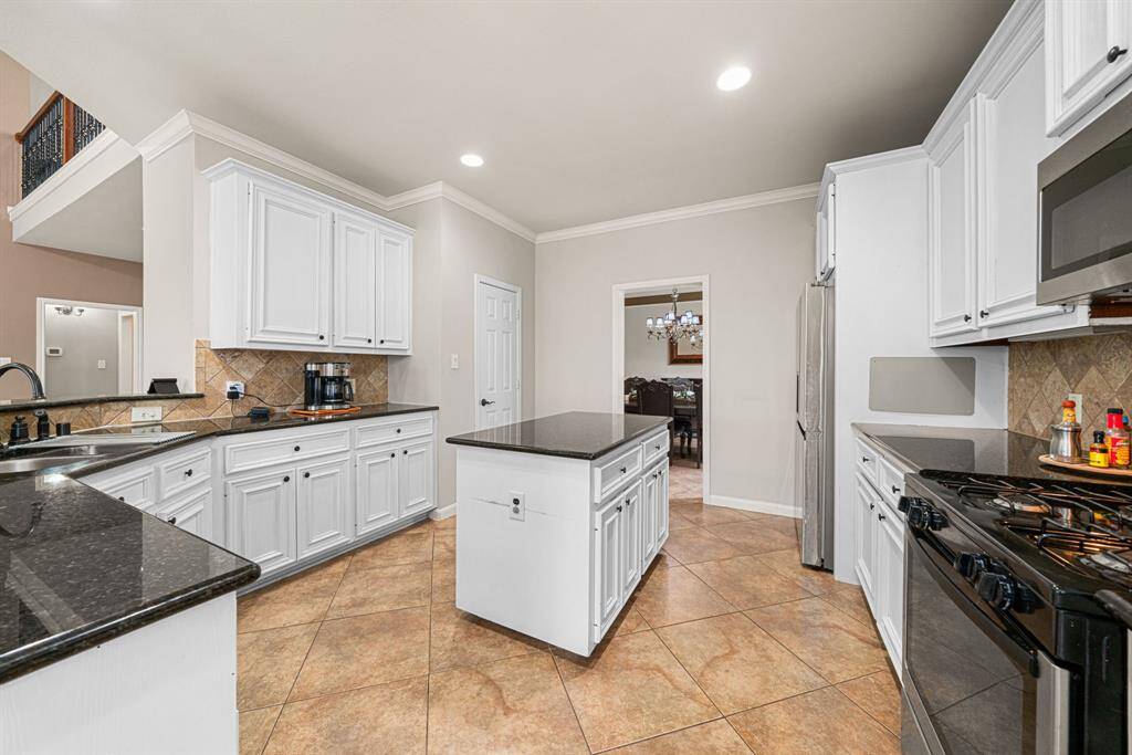 This expansive kitchen features a generous center island and bar seating, premium stainless steel appliances, and elegant granite countertops complemented by a stylish tile backsplash. Designed for both functionality and entertaining, the space offers abundant counter space and ample cabinetry storage. The open-concept layout flows seamlessly into the breakfast room and formal dining area, while the island overlooks the spacious living room—perfect for hosting gatherings. Large Walk-in Pantry