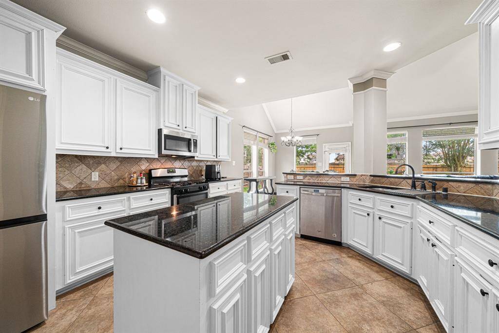 This expansive kitchen features a generous center island and bar seating, premium stainless steel appliances, and elegant granite countertops complemented by a stylish tile backsplash. Designed for both functionality and entertaining, the space offers abundant counter space and ample cabinetry storage. The open-concept layout flows seamlessly into the breakfast room and formal dining area, while the island overlooks the spacious living room—perfect for hosting gatherings.