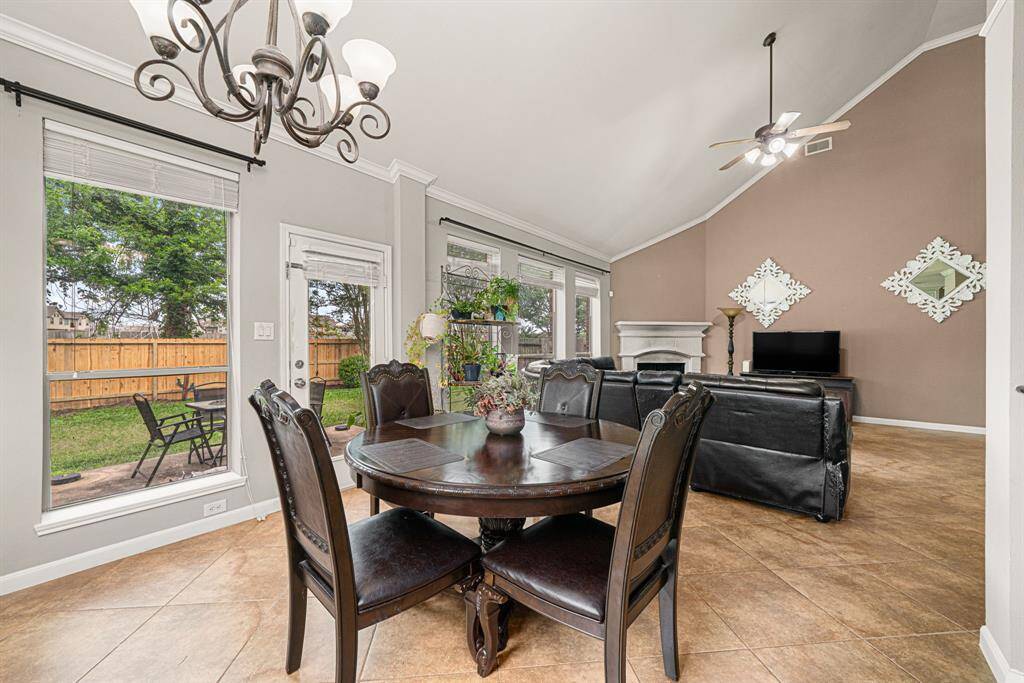 This expansive breakfast area features walls of windows showcasing backyard views and direct outdoor access, creating a bright and inviting atmosphere. The space is accentuated by upgraded iron light fixtures and elegant crown molding, with durable tile flooring extending throughout. Designed for effortless entertaining, the breakfast room flows seamlessly into the adjoining living room and kitchen, offering a perfect blend of natural light and functional elegance.