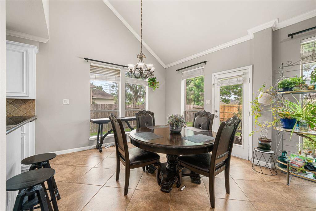 This expansive breakfast area features walls of windows showcasing backyard views and direct outdoor access, creating a bright and inviting atmosphere. The space is accentuated by upgraded iron light fixtures and elegant crown molding, with durable tile flooring extending throughout. Designed for effortless entertaining, the breakfast room flows seamlessly into the adjoining living room and kitchen, offering a perfect blend of natural light and functional elegance.