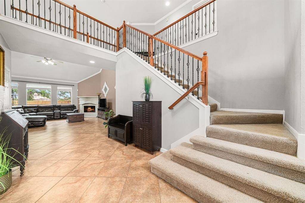 This impressive foyer features a gracefully curved staircase with elegant metal and wood banisters, creating a striking architectural focal point. The second-floor balcony overlooks both the dramatic two-story entrance and the adjacent living and dining areas, bathing the space in natural light for a bright, airy ambiance.