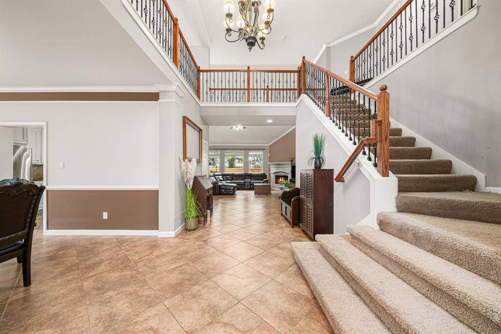This impressive foyer features a gracefully curved staircase with elegant metal and wood banisters, creating a striking architectural focal point. The second-floor balcony overlooks both the dramatic two-story entrance and the adjacent living and dining areas, bathing the space in natural light for a bright, airy ambiance.