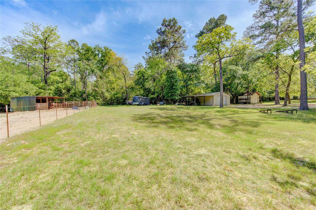This spacious property features a large, open grassy area surrounded by mature trees, offering shade and privacy. There are multiple outbuildings, including a fenced area suitable for animals. Ideal for those seeking a blend of nature and utility.