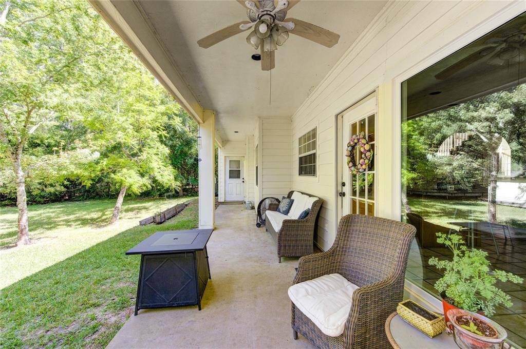 This photo features a cozy covered patio with seating, a ceiling fan, and a view of a lush, green backyard, ideal for relaxation and outdoor entertaining.