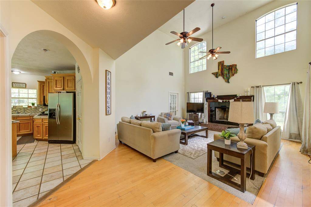 This spacious living area features high ceilings with large windows for natural light, a cozy fireplace, and an open layout leading to a modern kitchen with stainless steel appliances. Perfect for family gatherings and entertaining.