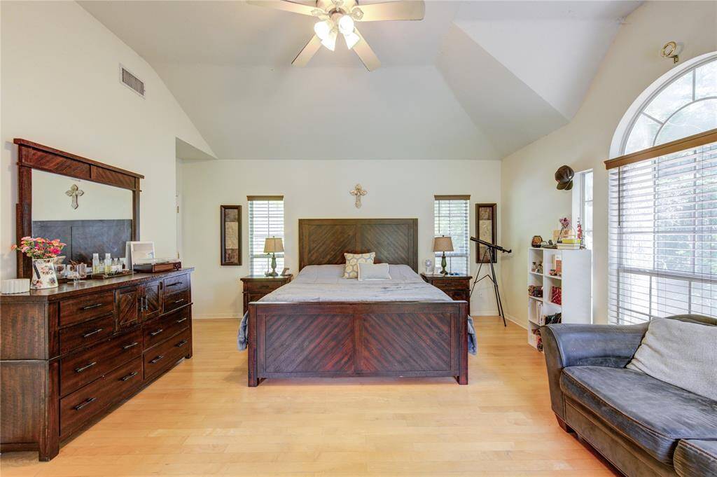 Spacious bedroom with vaulted ceilings, featuring a large bed, wooden furniture, and a cozy seating area. Natural light streams in through an arched window, creating a bright, inviting atmosphere.