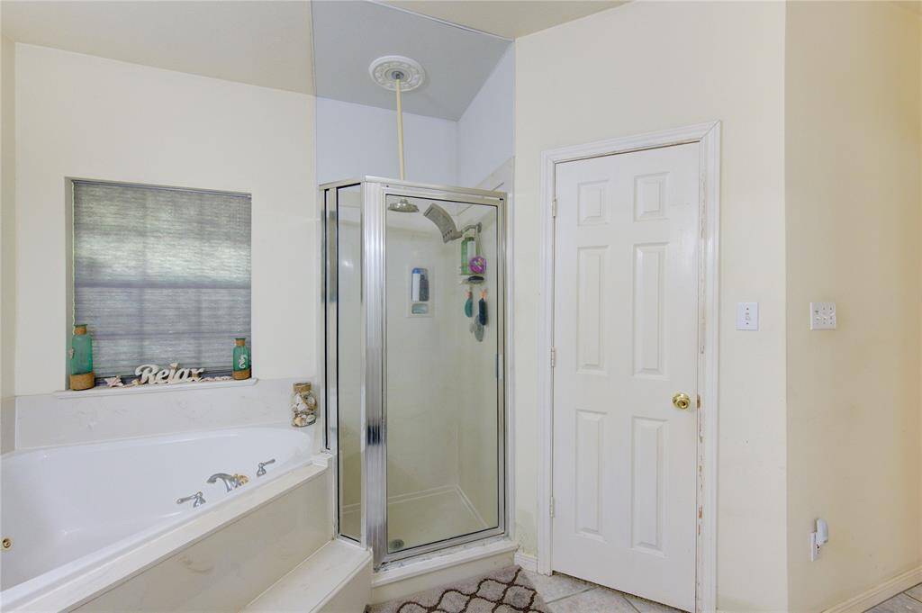This bathroom features a cozy corner with a jetted tub and a separate glass-enclosed shower. A window above the tub provides natural light, and there's a simple, neutral color scheme.