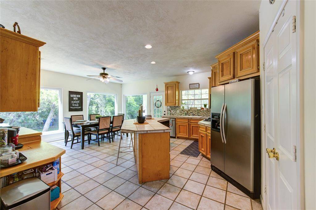 This spacious kitchen features wooden cabinetry, a large island, and stainless steel appliances. It opens to a bright dining area with large windows and scenic outdoor views, creating a welcoming and functional space for cooking and entertaining.