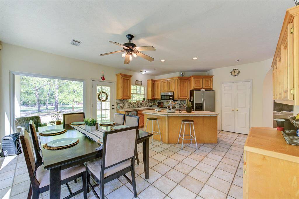 Bright and spacious kitchen with wooden cabinetry, stainless steel appliances, and a central island. Adjacent dining area features large windows and a door leading to a scenic outdoor view, enhancing natural light. Perfect for family gatherings and entertaining.