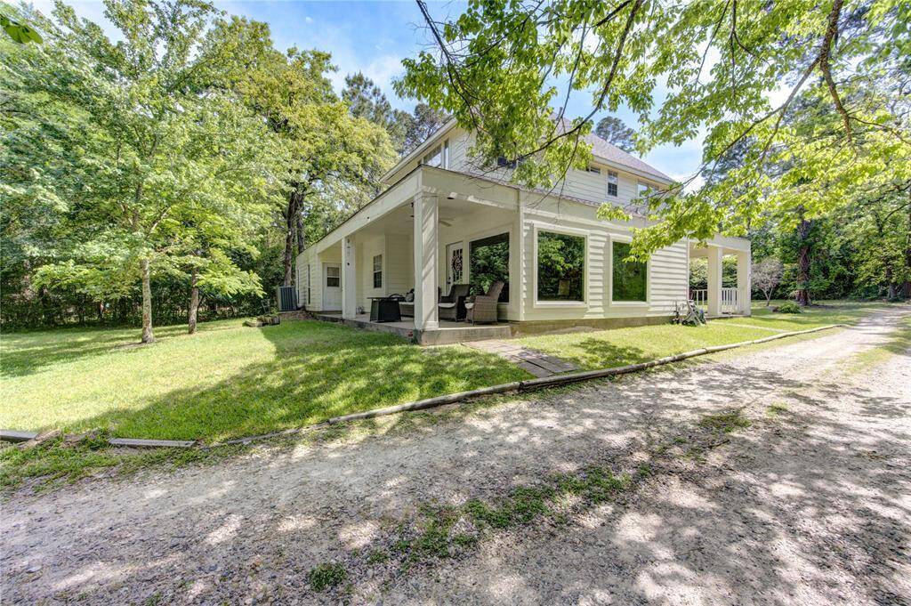Charming two-story home with a spacious covered porch, nestled in a lush, wooded setting. It features a well-maintained yard and ample natural light through large windows, offering a serene and private atmosphere.