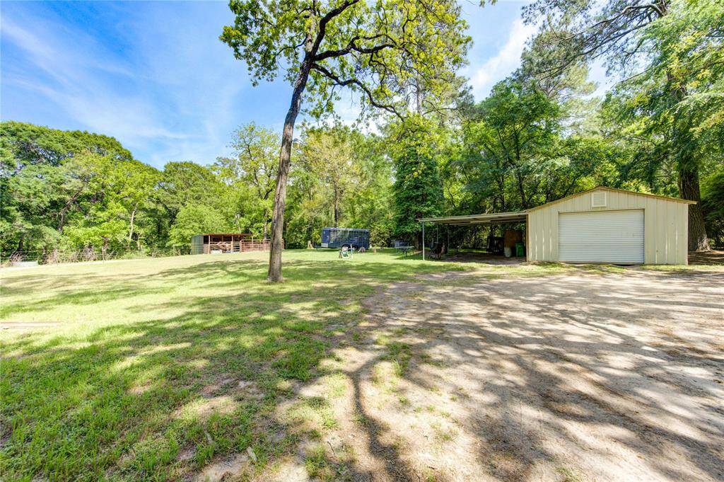 Spacious outdoor area featuring a large metal shed and carport, surrounded by lush greenery and mature trees, providing a serene and private setting.