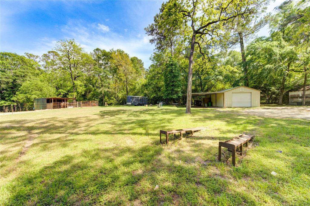 A spacious, grassy yard with mature trees, featuring a shed and a covered storage area. Ideal for outdoor activities and storage, surrounded by nature for a serene setting.