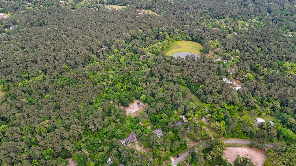 The photo shows a vast, forested area with scattered homes and a small pond, offering a serene and private setting ideal for nature lovers seeking tranquility and space.
