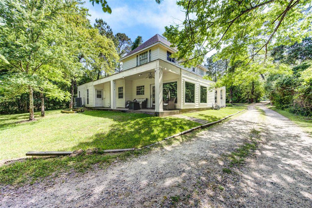 This charming two-story home features a spacious wrap-around porch, large windows, and is surrounded by lush greenery, offering a serene and private setting. A long gravel driveway adds to the rustic appeal and provides ample parking space.