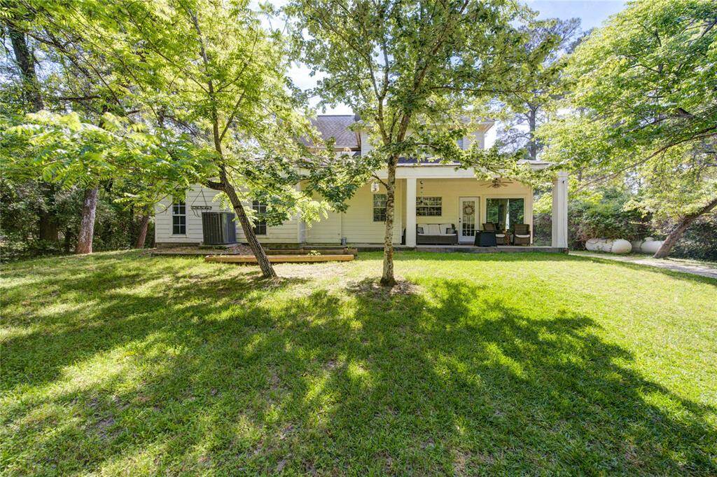 This photo shows a charming house with a spacious, lush backyard. It features a covered patio area, surrounded by mature trees, offering a serene and private outdoor space ideal for relaxation and entertainment.