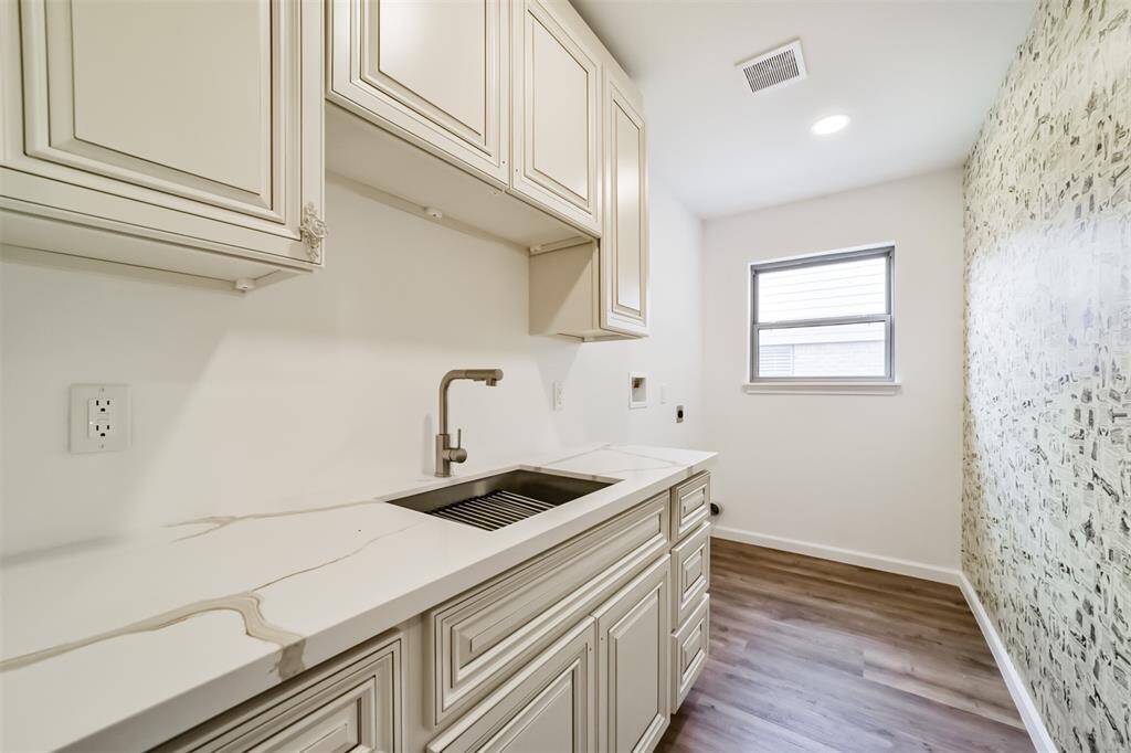 Laundry room located in hallway features upper and lower cabinets for storage and a sink.