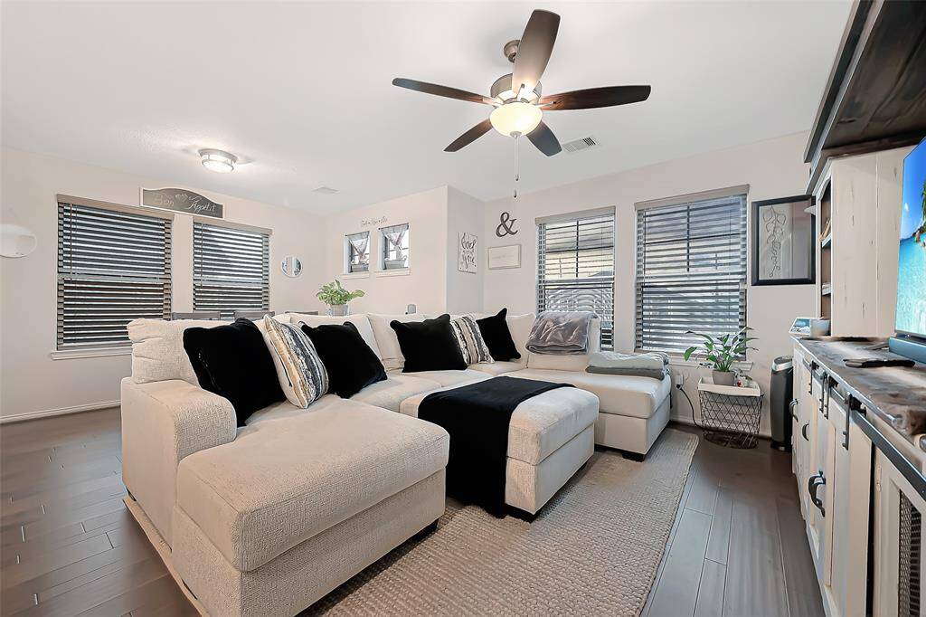 Spacious living area filled with natural light, featuring sleek wood-look flooring and a modern ceiling fan.