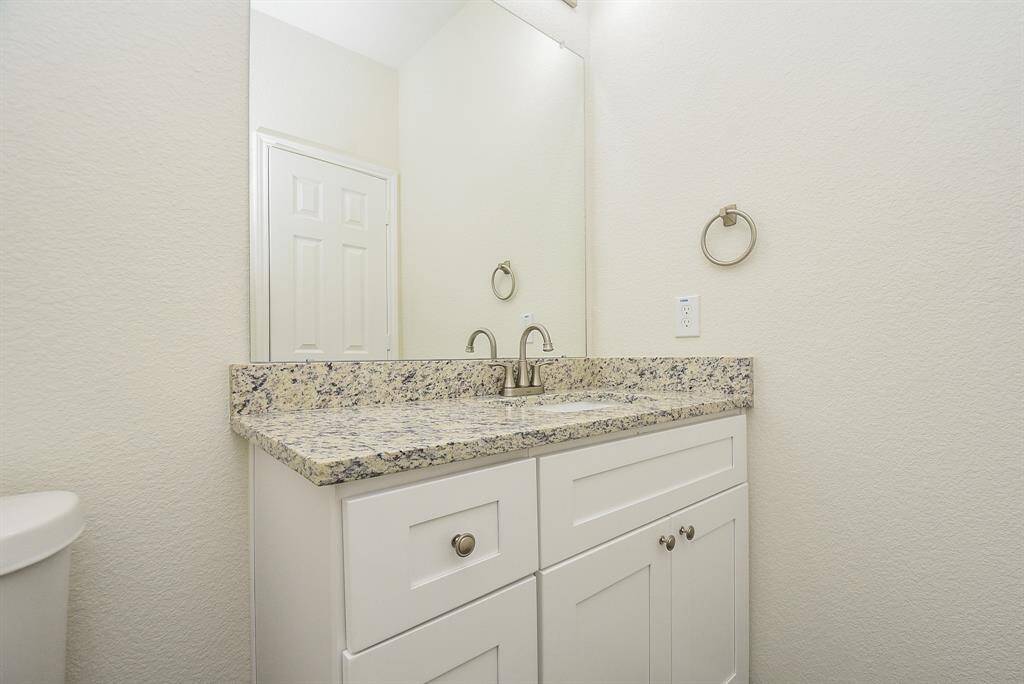 A clean, white bathroom with a granite countertop, white cabinets, a mirror, and modern fixtures.