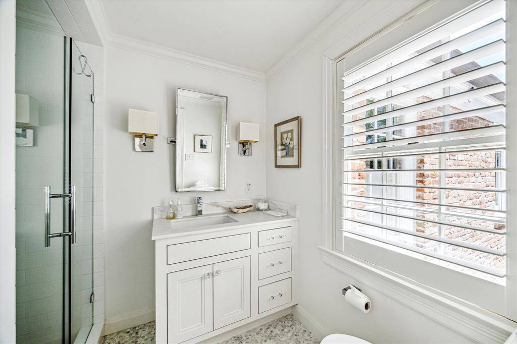 Crisp and polished, this secondary bathroom features a stone-topped vanity, a frameless glass shower, and elegant sconces that elevate the classic design. Plantation shutters provide both privacy and charm.