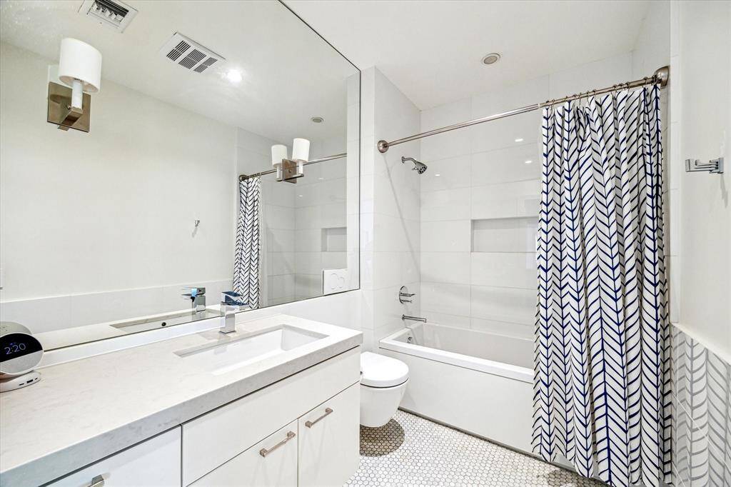 Fresh and modern, this secondary bathroom features a sleek vanity with quartz countertops, a large mirrored wall, and classic penny tile flooring. The tub-shower combo with built-in niche adds functionality and clean-lined appeal.