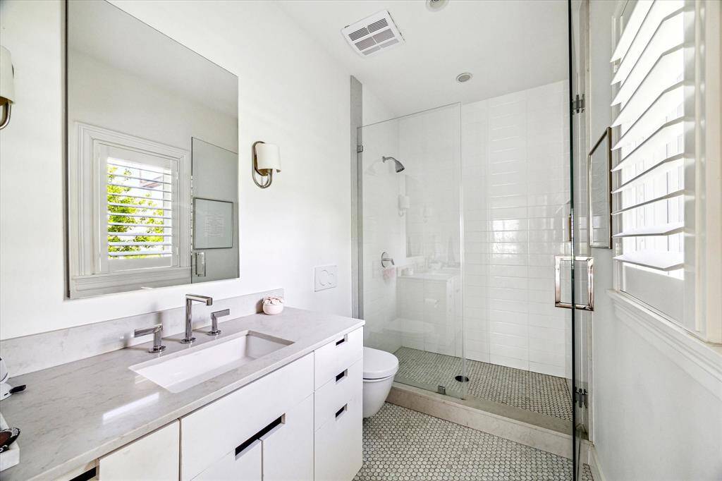 Clean lines and a soft neutral palette define this secondary bathroom, featuring a quartz-topped vanity, polished chrome fixtures, and a glass-enclosed shower. Classic penny tile flooring and natural light complete the fresh, modern look.