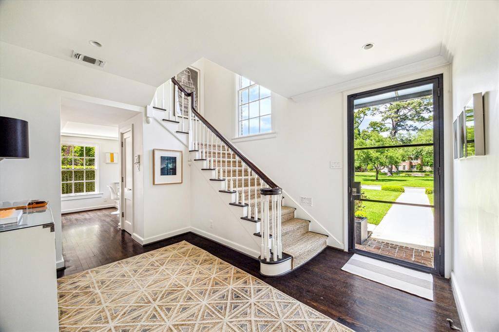 Bright, welcoming, and effortlessly elegant—the foyer sets the tone with rich hardwood floors, crisp white walls, and a timeless staircase bathed in natural light from oversized windows. The steel and glass front door offers a stylish first impression and a picturesque view of Chevy Chase Drive.