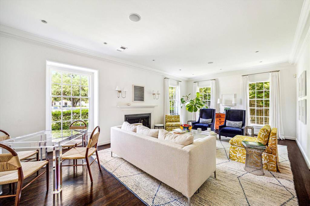 Bathed in natural light from walls of tall windows, the formal living room offers a serene and airy atmosphere accented by crisp millwork, rich hardwood floors, and a classic fireplace that anchors the space with timeless elegance.
