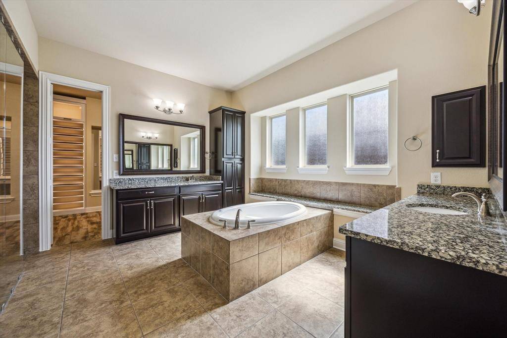 Indulge in the elegant owner's retreat with an en-suite bath, featuring dual vanities, framed mirrors, a luxurious soaking tub, and stylish tile flooring.