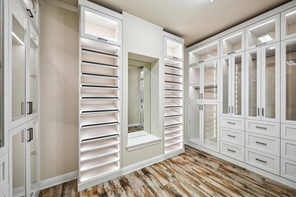Indulge in a luxurious custom walk-in closet featuring abundant storage, elegant lighting, and a built-in mirror with a handy alterations space.