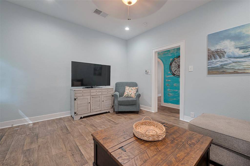 This cozy living room features soft blue walls, wood flooring, and a ceiling fan. Ample natural light streams through the windows, creating a welcoming atmosphere.
