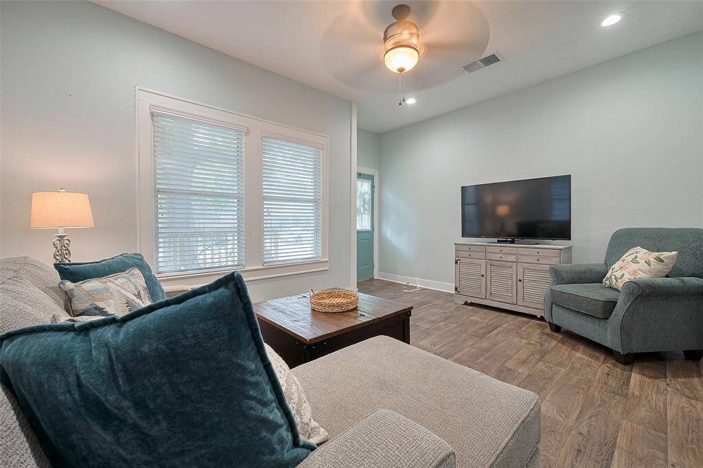 This cozy living room features soft blue walls and wood-look flooring. A ceiling fan provides air circulation, while large windows allow natural light to brighten the space.