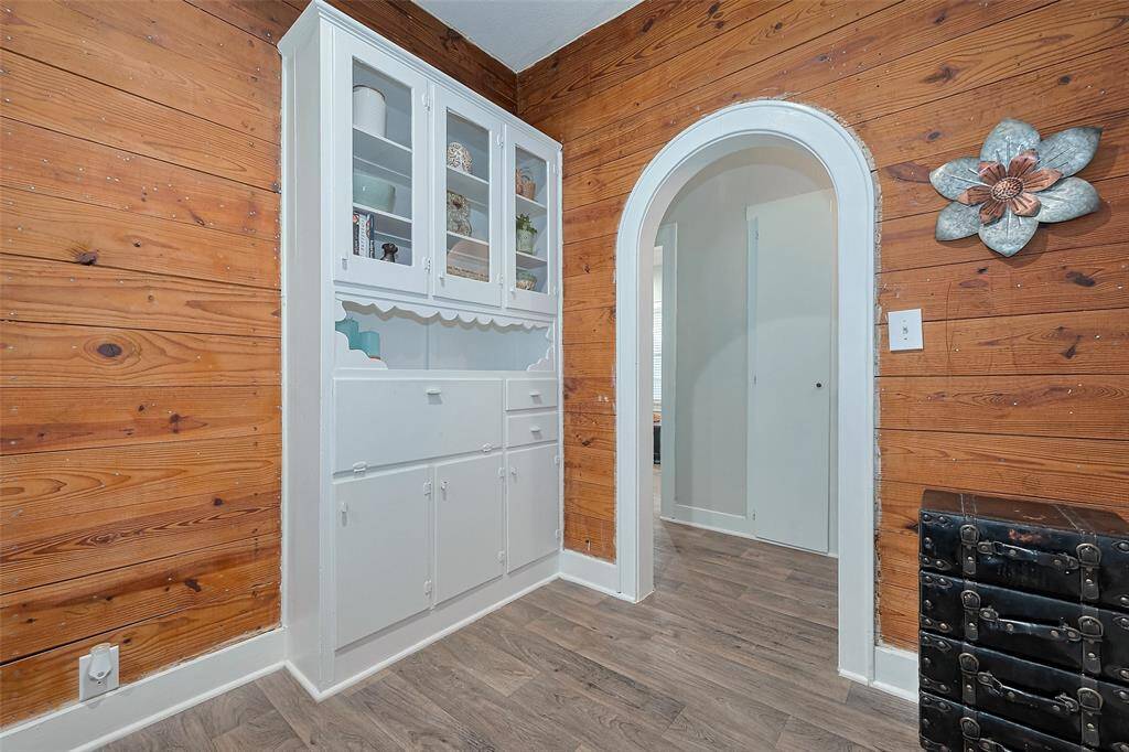 Charming room with warm wood-paneled walls and a built-in white cabinet perfect for storage and display. An arched doorway adds vintage character, while light wood flooring ties the space together with rustic charm.