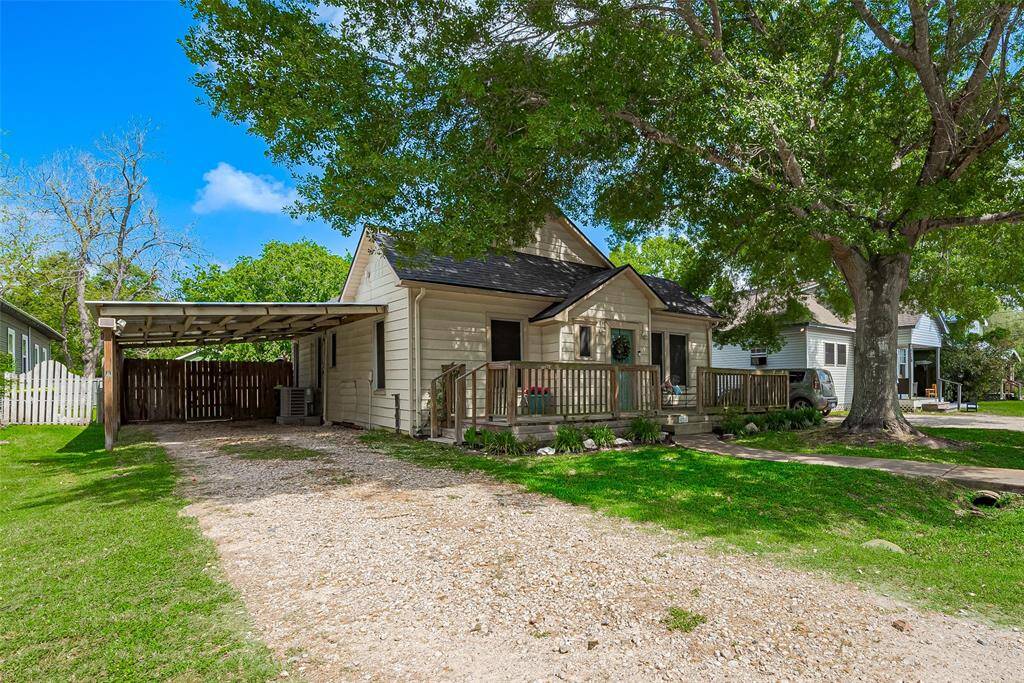 Charming single-story home with a welcoming front porch, nestled under mature trees. It features a gravel driveway with a covered carport and a fenced backyard. Ideal for those seeking a cozy residence in a serene neighborhood.