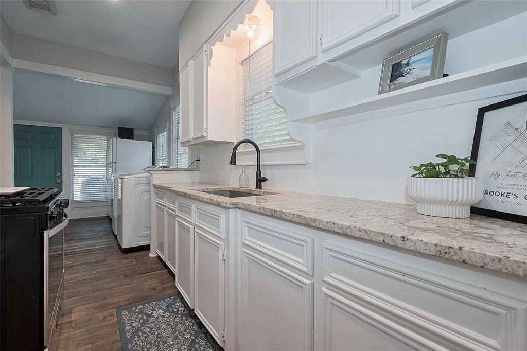 This photo showcases a bright galley kitchen with white cabinetry and light granite countertops. A stylish updated faucet, ample storage, and windows that let in natural light make the space both functional and inviting.
