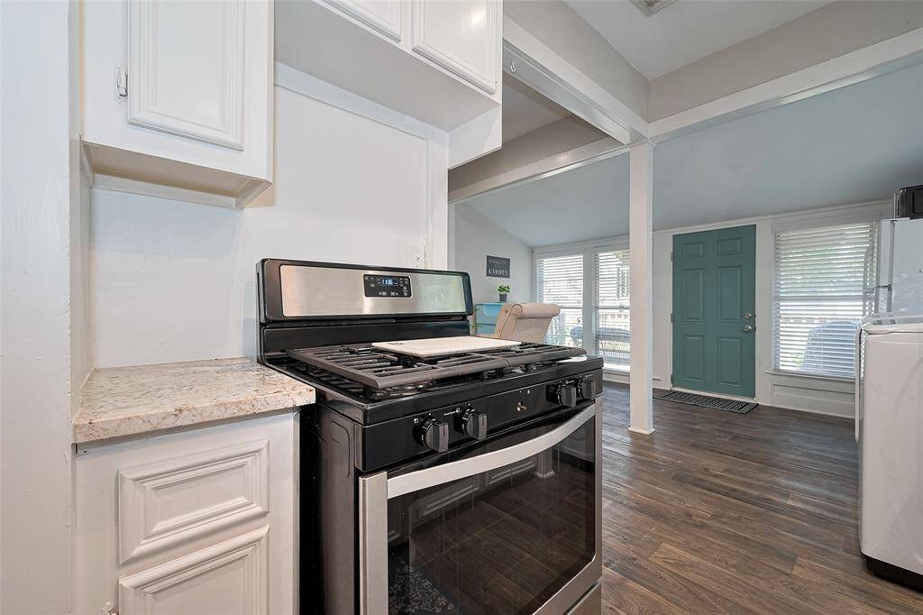 Modern kitchen featuring stainless steel appliances and granite countertops, seamlessly opening into a bright living area with large windows and a charming teal front door.