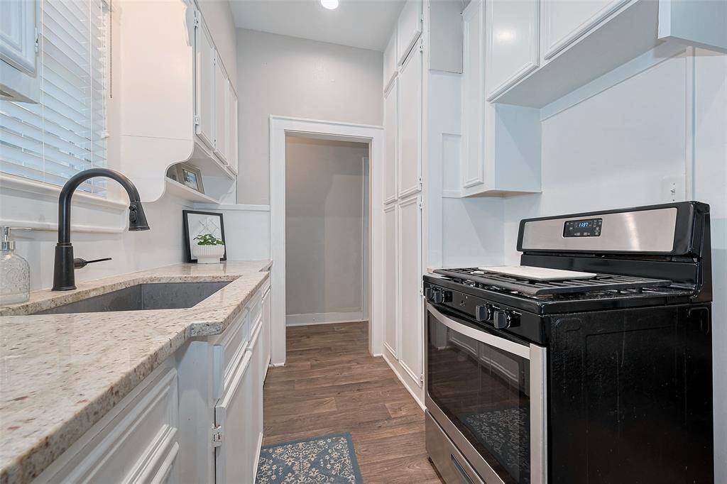 This photo showcases a bright galley kitchen with white cabinetry and light granite countertops. A stylish updated faucet and ample storage.