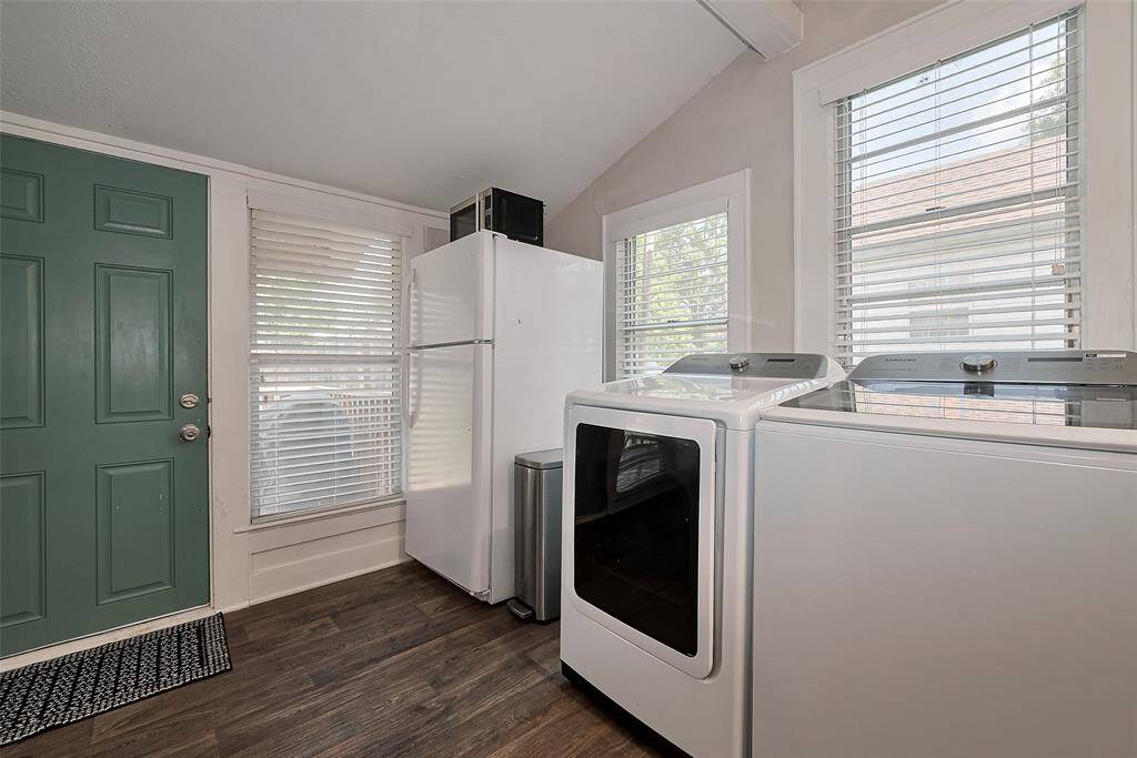 This photo shows a bright laundry room with a modern washer and dryer, a full-sized refrigerator, and large windows providing ample natural light.