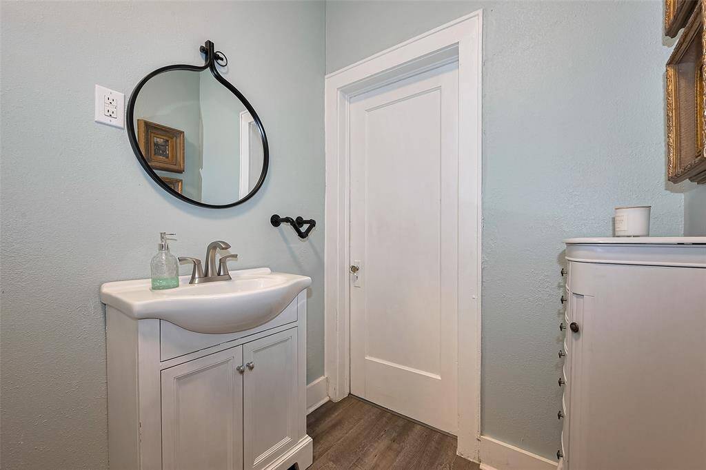 Fully remodeled bathroom featuring grey wood-look flooring and an updated bathtub-shower combo with dual shower heads and a built-in shelf. Black detail accents throughout add a modern touch.