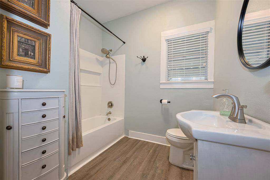 Fully remodeled bathroom featuring grey wood-look flooring and an updated bathtub-shower combo with dual shower heads and a built-in shelf. Black detail accents throughout add a modern touch.