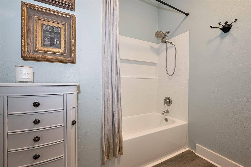 Fully remodeled bathroom featuring grey wood-look flooring and an updated bathtub-shower combo with dual shower heads and a built-in shelf. Black detail accents throughout add a modern touch.