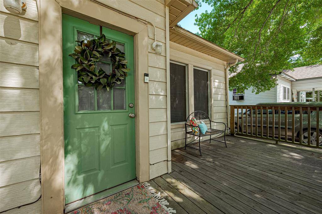 Charming front porch with a welcoming front door. The spacious wooden deck is perfect for relaxing under the shade of nearby trees. Ideal for enjoying outdoor moments.