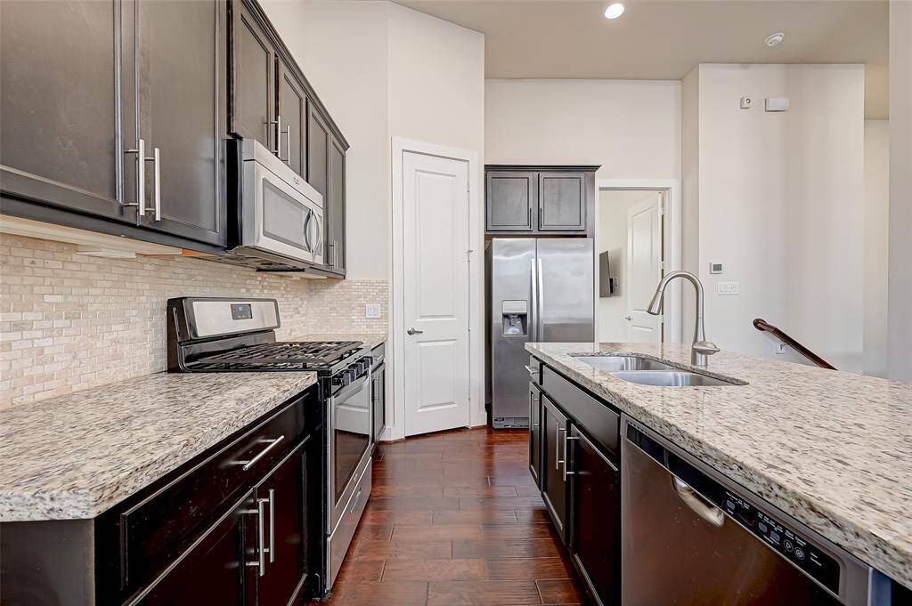 This view of the kitchen highlights the large island with bar seating, stainless steel appliances, and a sleek, modern backsplash that adds a stylish touch. A spacious pantry offers plenty of storage, making this kitchen as practical as it is beautiful.