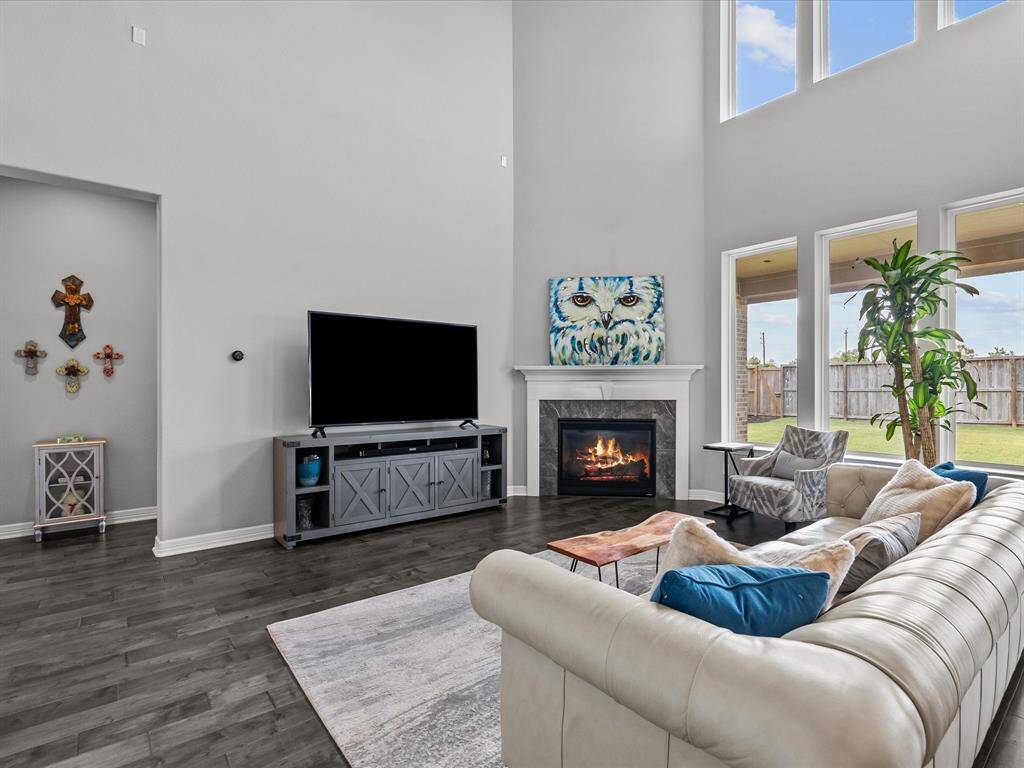 The living room open to the kitchen features wood flooring, two-story high ceilings, a wall of windows and a cozy fireplace for those cold winter nights