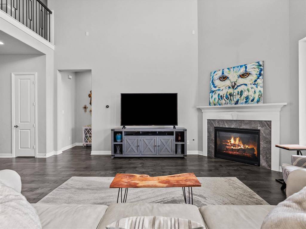 The living room open to the kitchen features wood flooring, two-story high ceilings, a wall of windows and a cozy fireplace for those cold winter nights