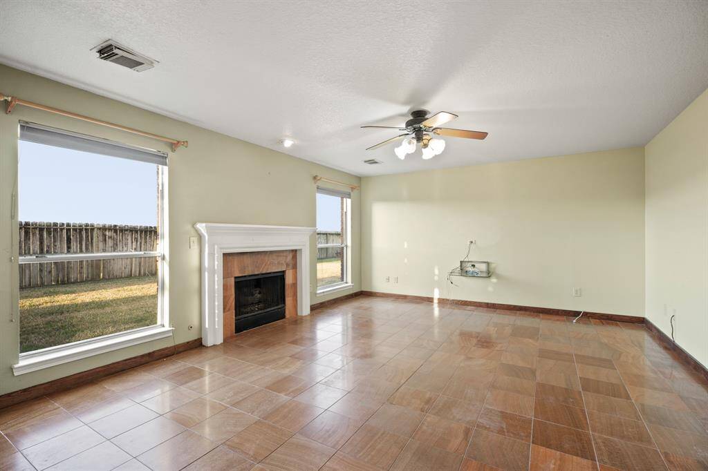 This spacious family room features large windows offering plenty of natural light, a cozy fireplace, and tiled flooring. The ceiling fan provides added comfort, and the room opens to a fenced backyard, perfect for relaxing or entertaining.