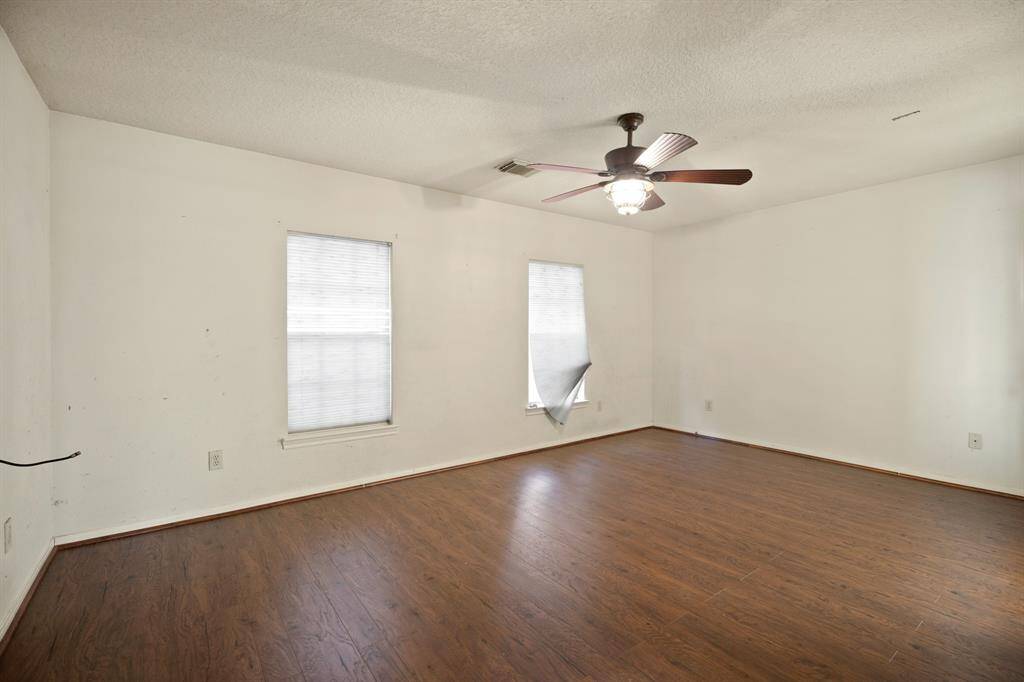 This huge primary room features luxury vinyl wood floors, two windows with blinds, and a ceiling fan. The walls are plain, offering a blank canvas for personalization.