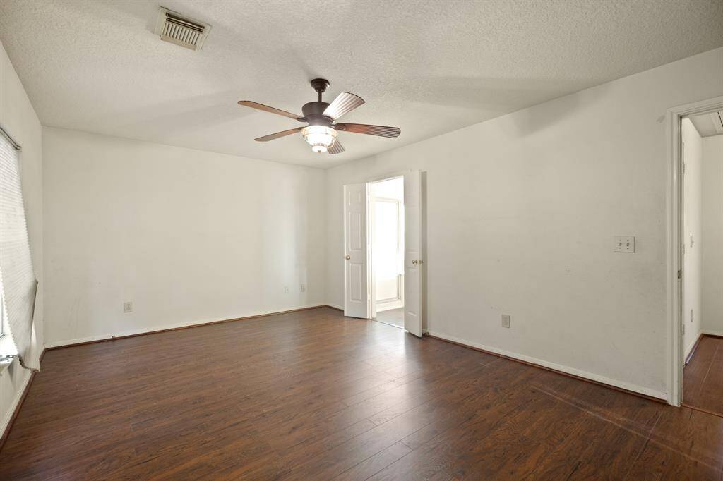 This room features wood flooring, neutral walls, and a ceiling fan, with a door leading to an adjacent space. It offers a spacious, versatile area with natural light from a window.
