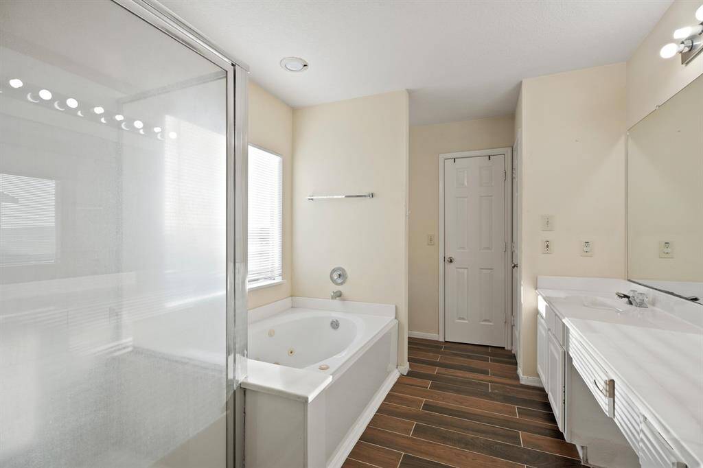 This bathroom features a sleek design with a glass-enclosed shower, a spacious bathtub, and dual sinks. The room is well-lit with modern fixtures and has stylish wood-look tile flooring.